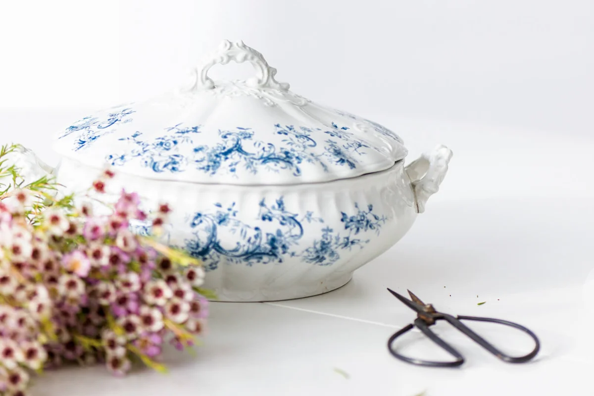 A vintage soup tureen on a white round table with wax fresh flowers