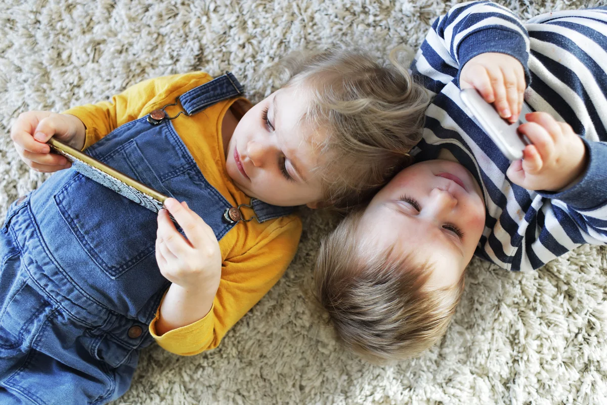 Brother and sister laying down looking at phones