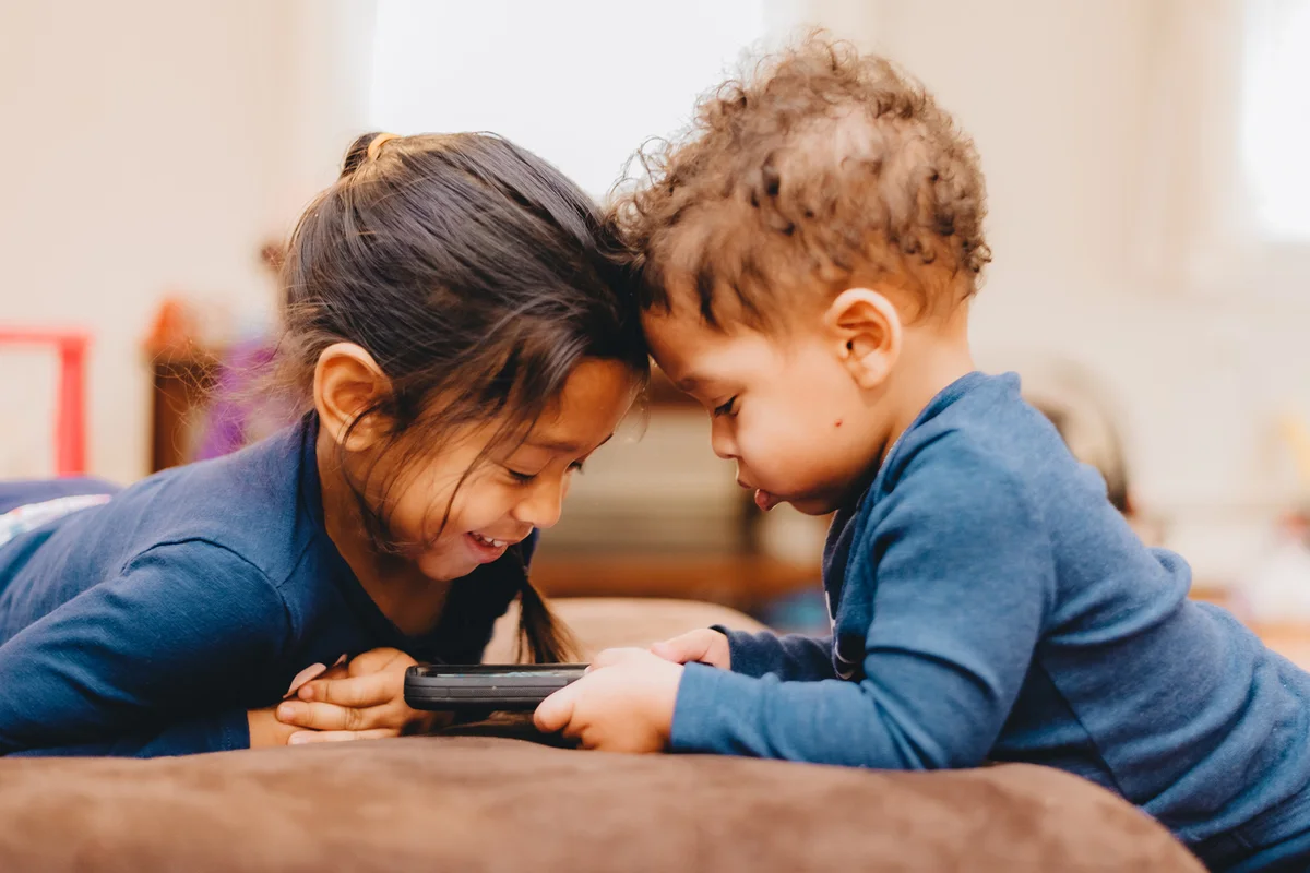 Baby Boy Using Smart Phone With Sister On Sofa
