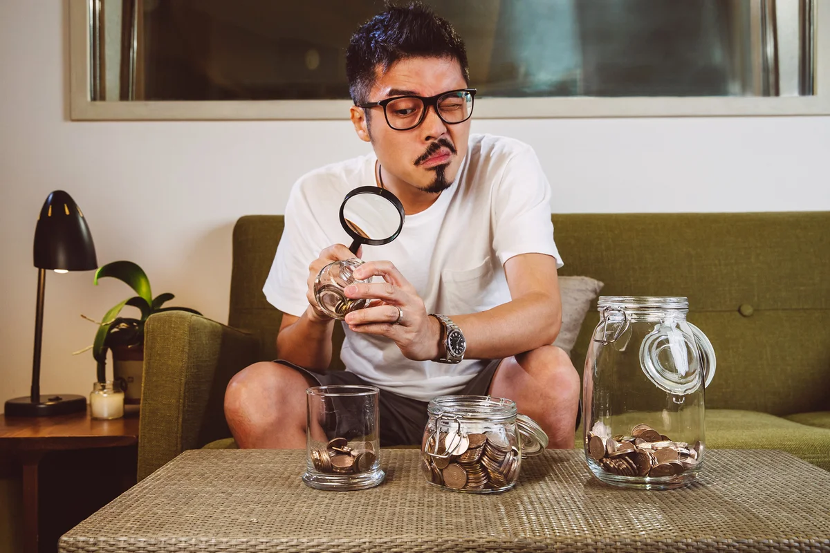 Man examining coins with magnifying glass at home