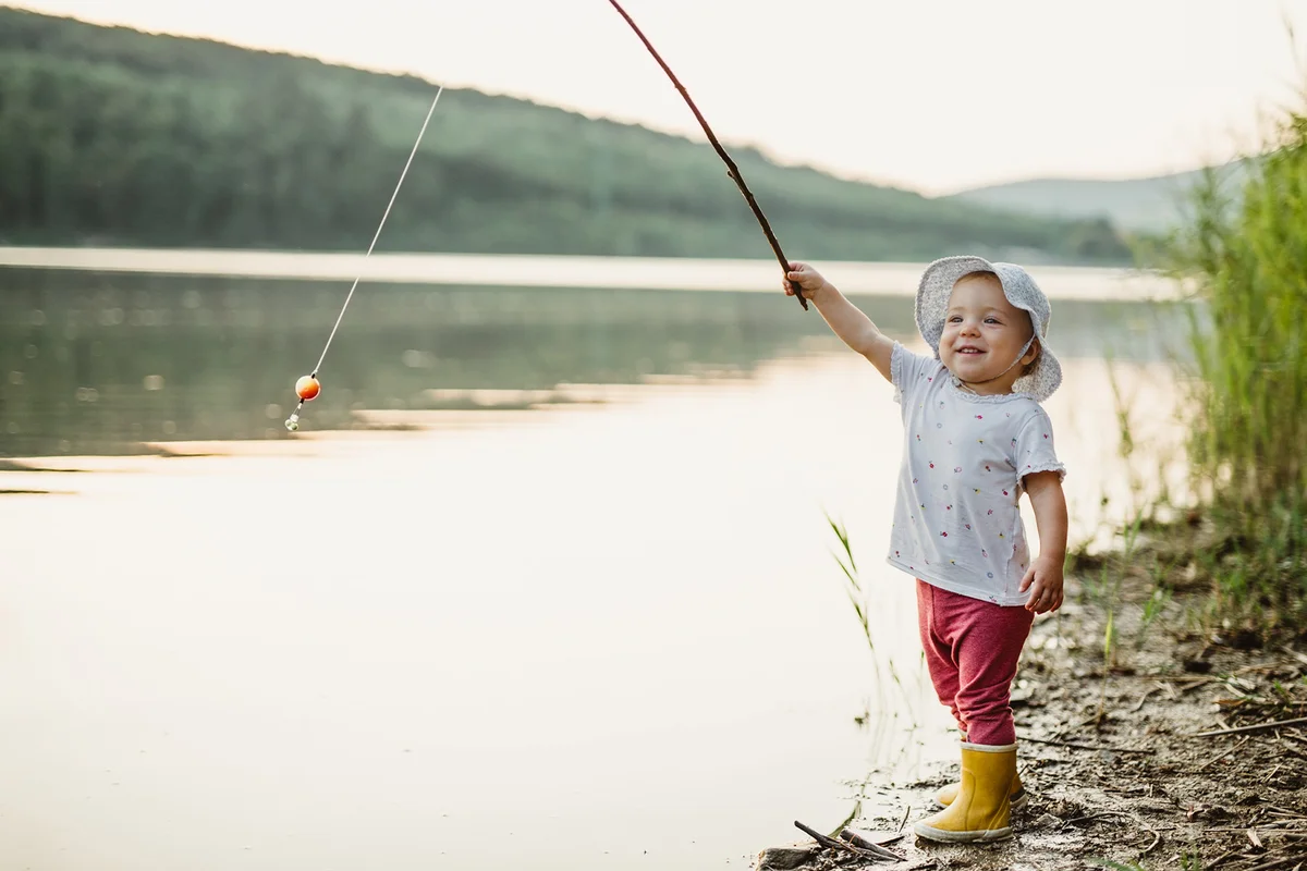 Toddler girl holding a fishing rod by a lake