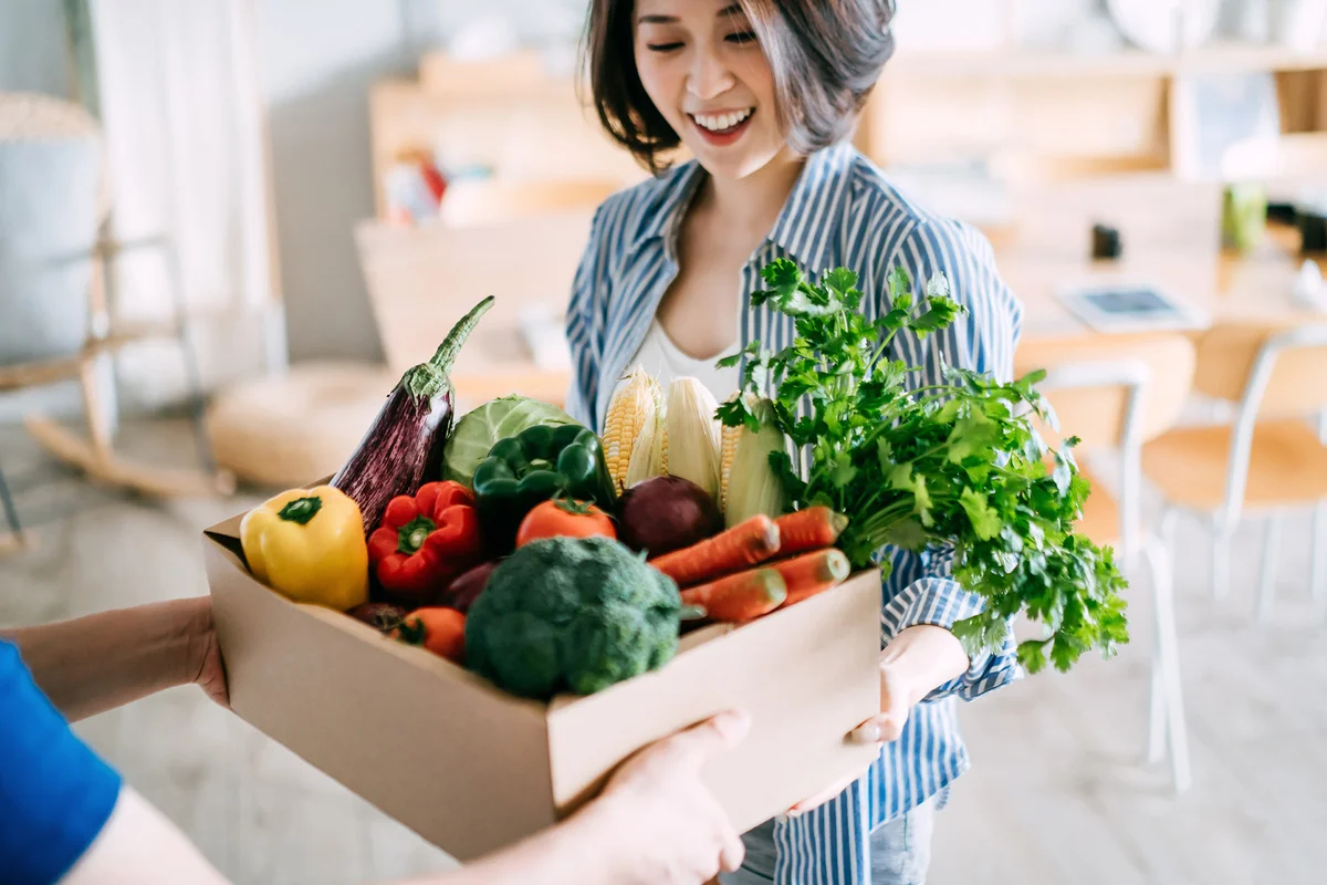 Woman receiving a box full of colourful and fresh organic groceries