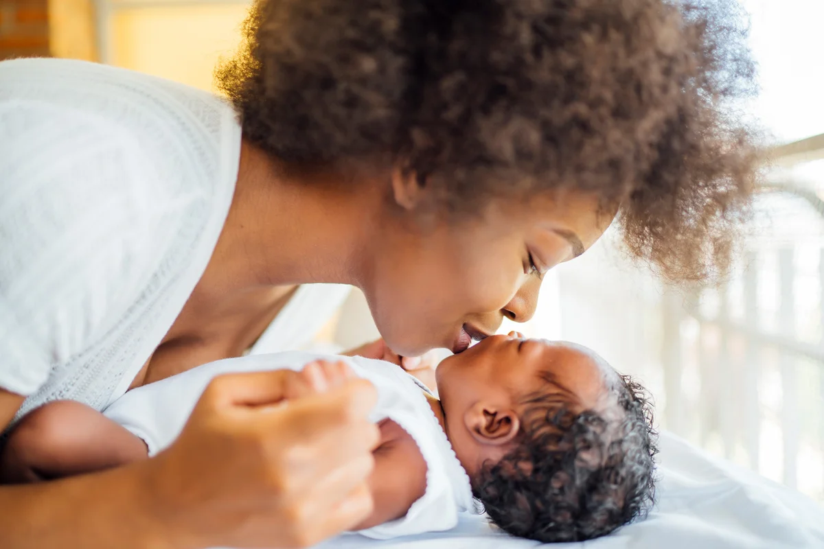 Mother kissing baby daughter lying on bed at home