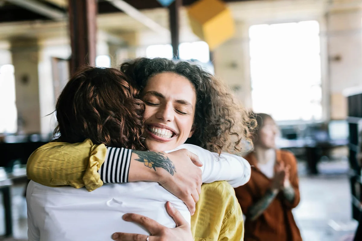 Woman is being hugged by one of her co-worker