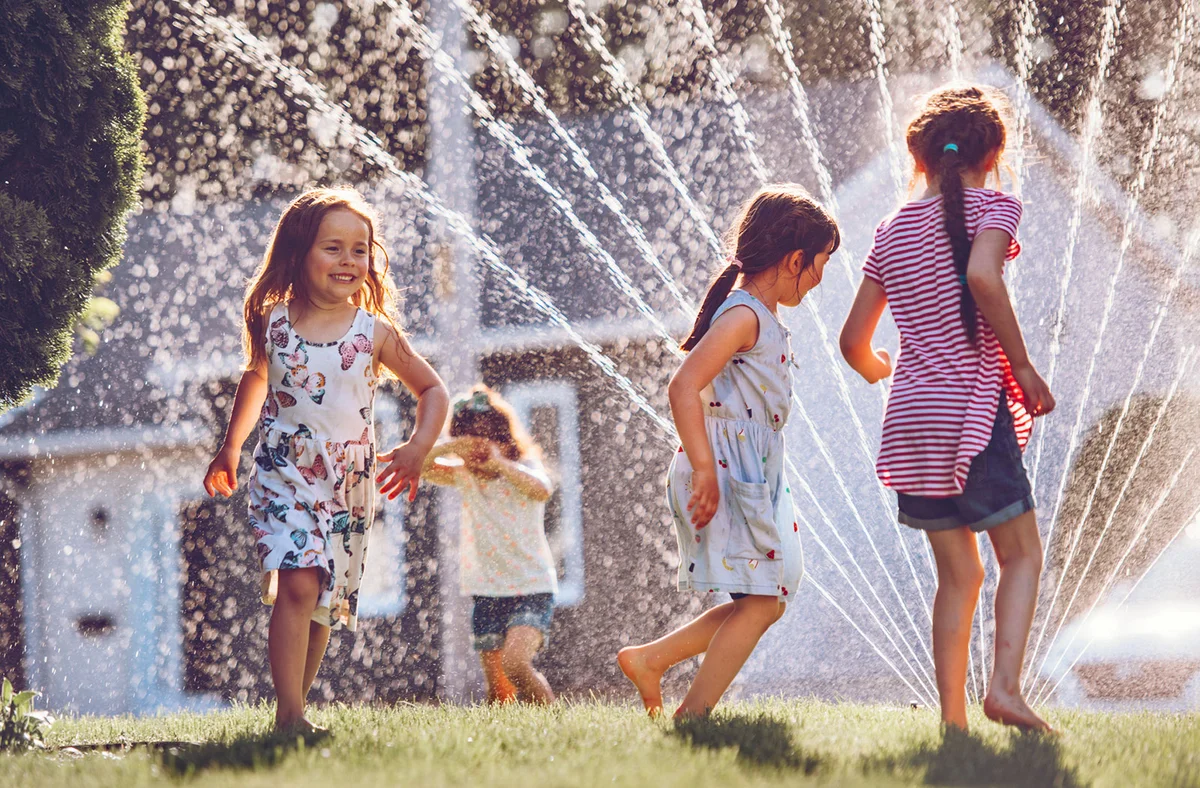 children running through water sprinkler in yard