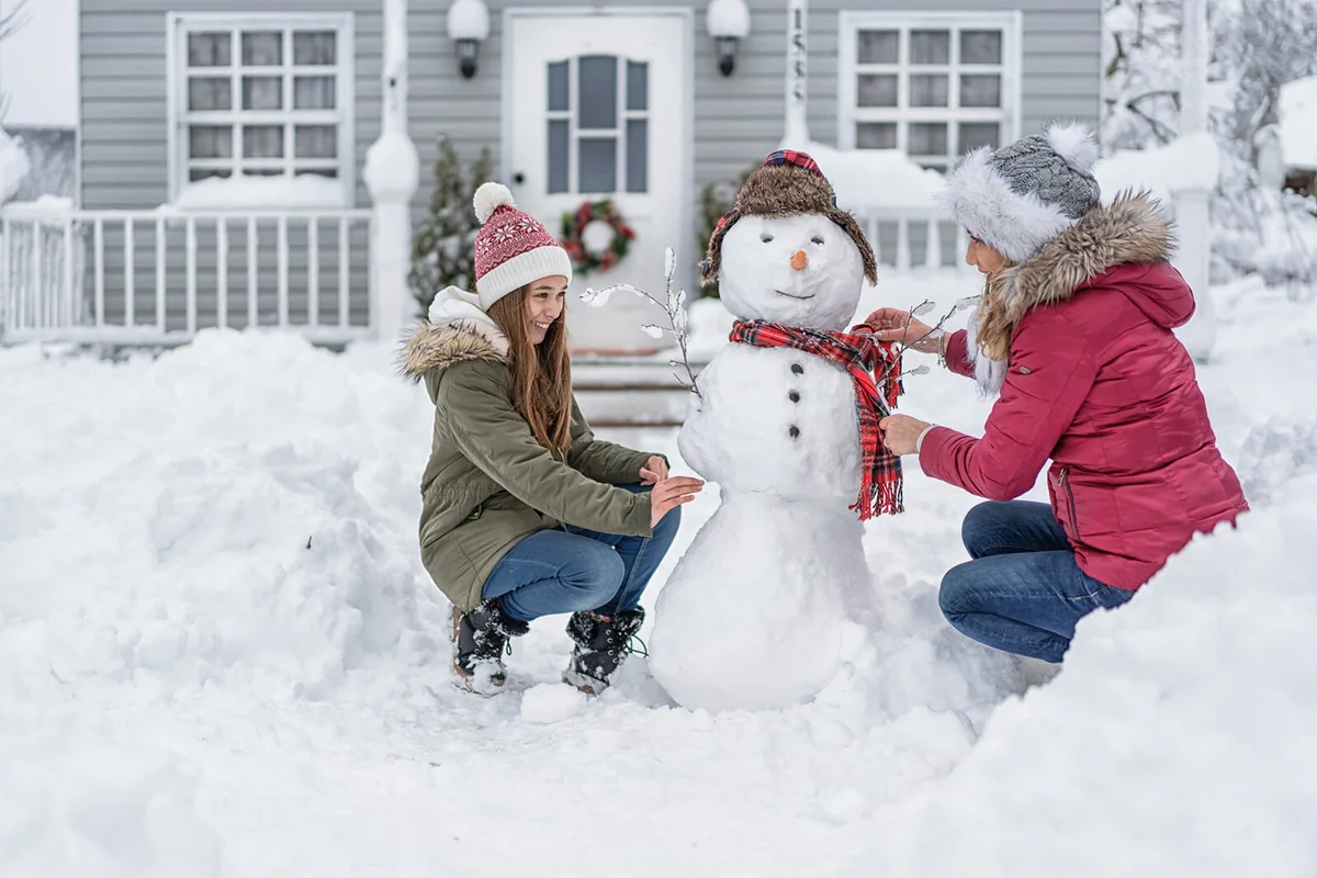 Mother and daughter making a snowman in front of the house