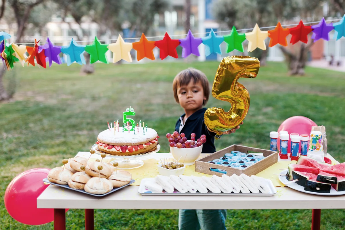 Little boy with golden balloon behind laid birthday table