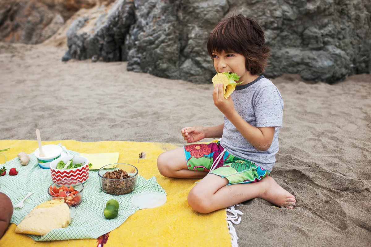 Boy eating taco while sitting on sand at beach