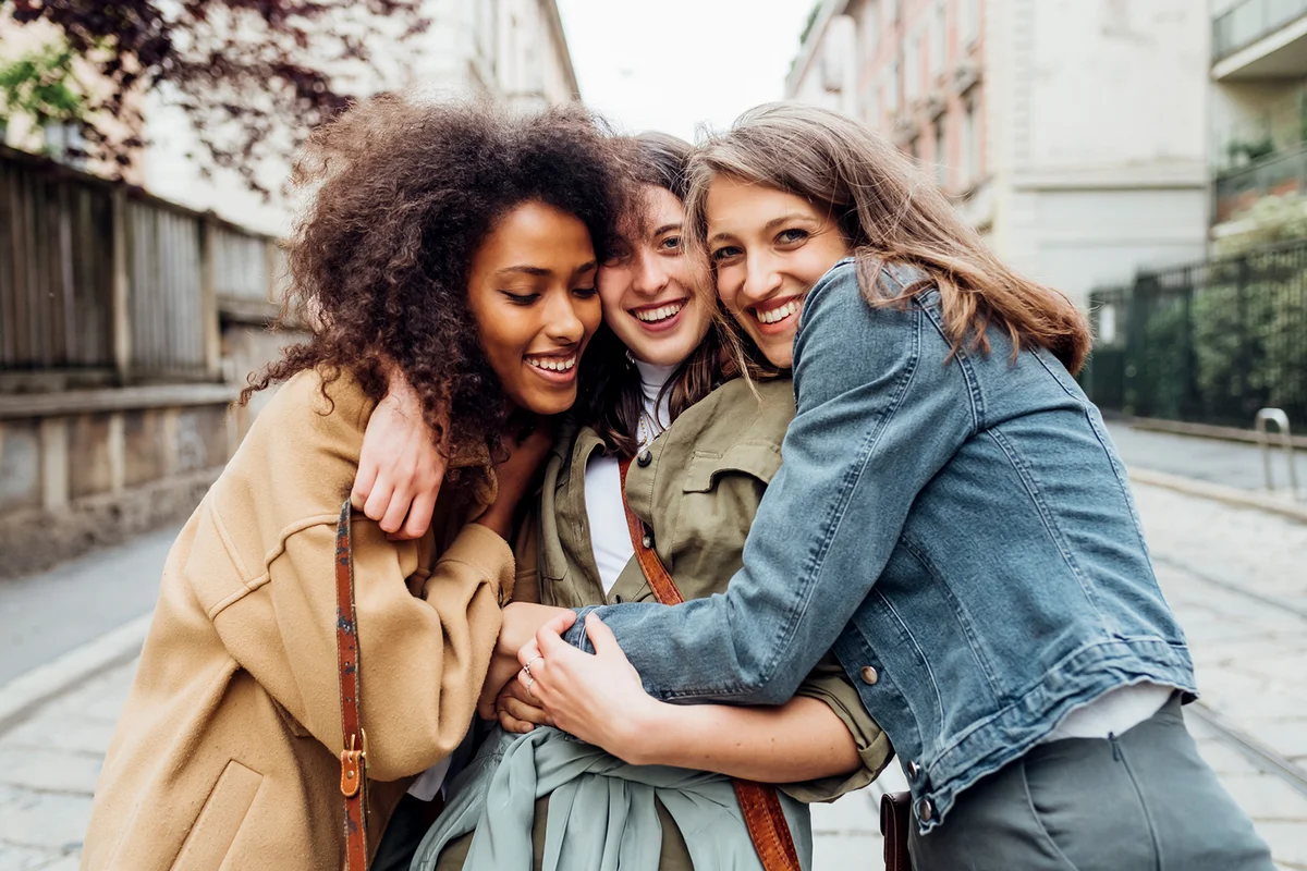 Happy friends embracing while standing on footpath