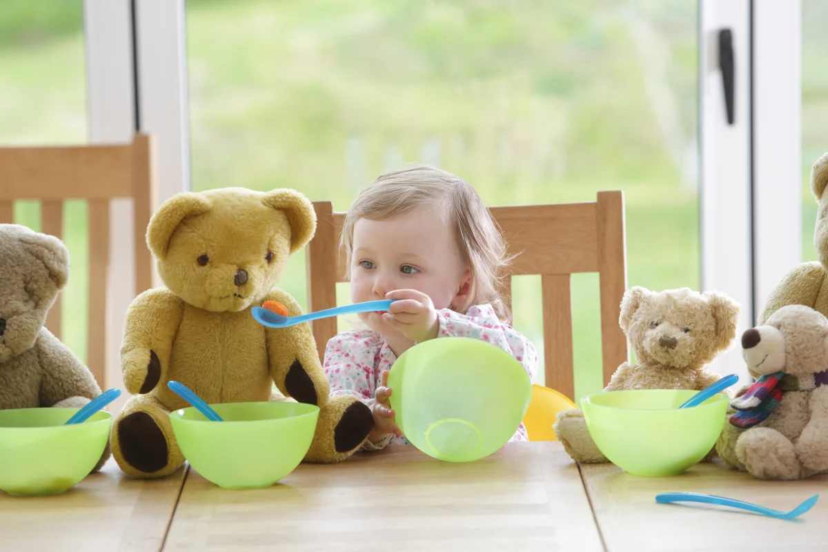 Toddler feeding teddy bears at table