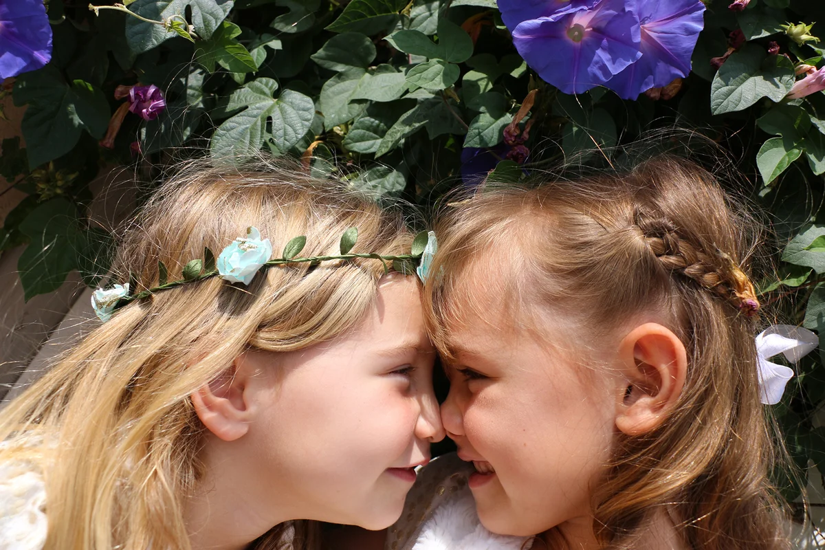 Two beautiful sisters laugh and play in front of beautiful purple flowers
