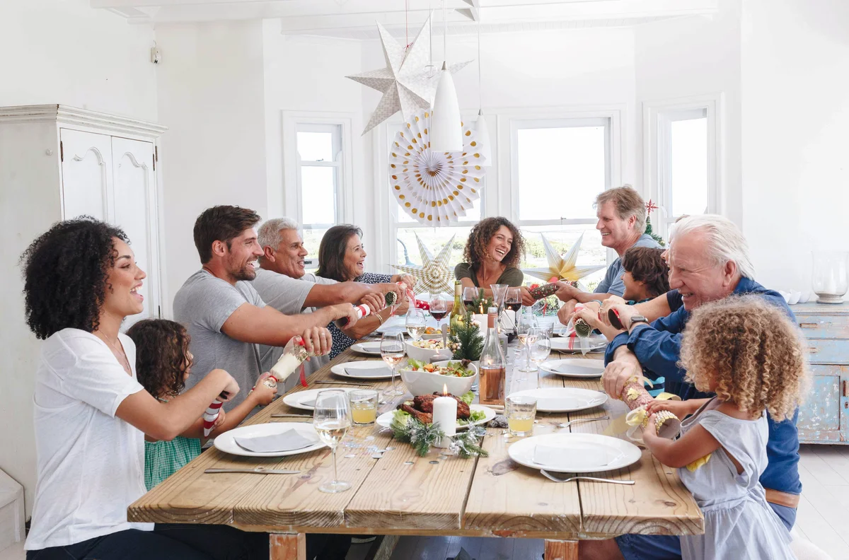Family popping Christmas crackers together at dining table