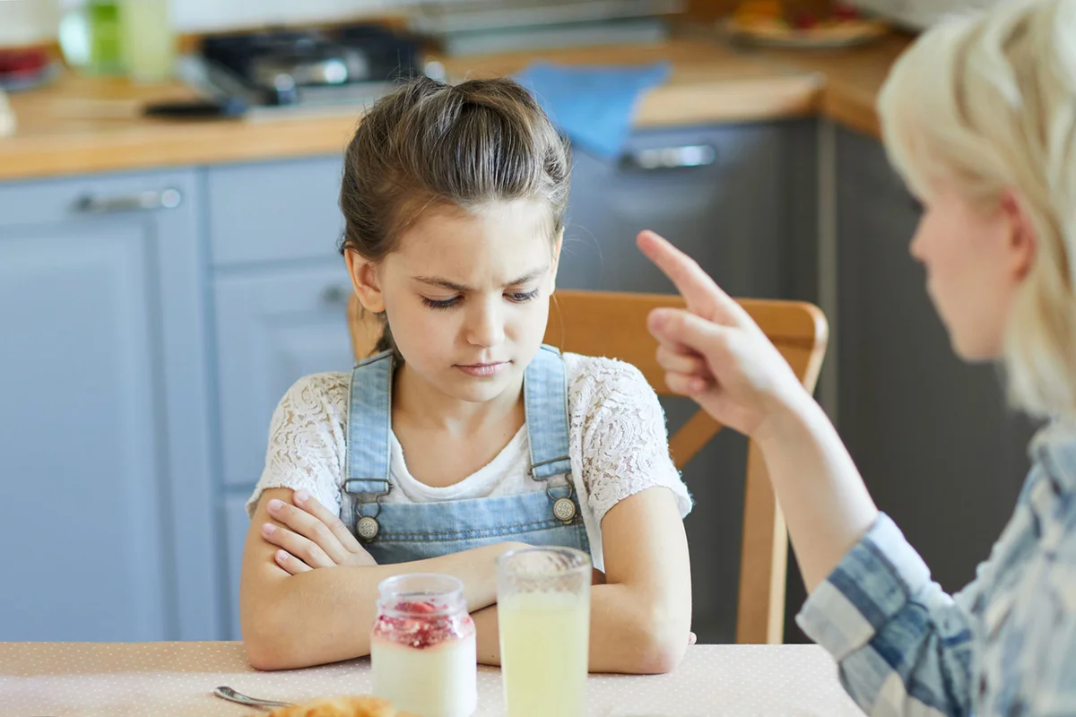 mother scolding sad daughter at dinner table