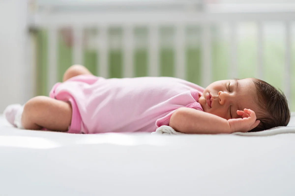 infant girl in pink onesie sleeping in crib