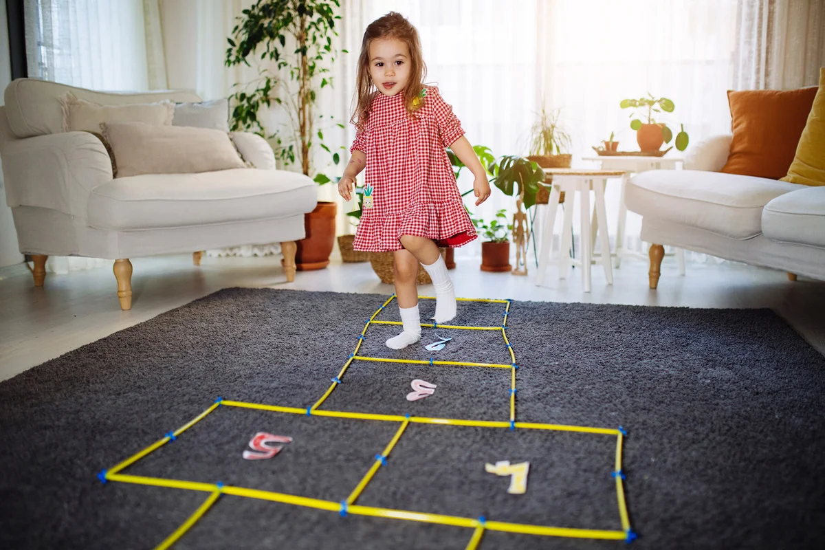 Toddler girl having fun playing hopscotch at home