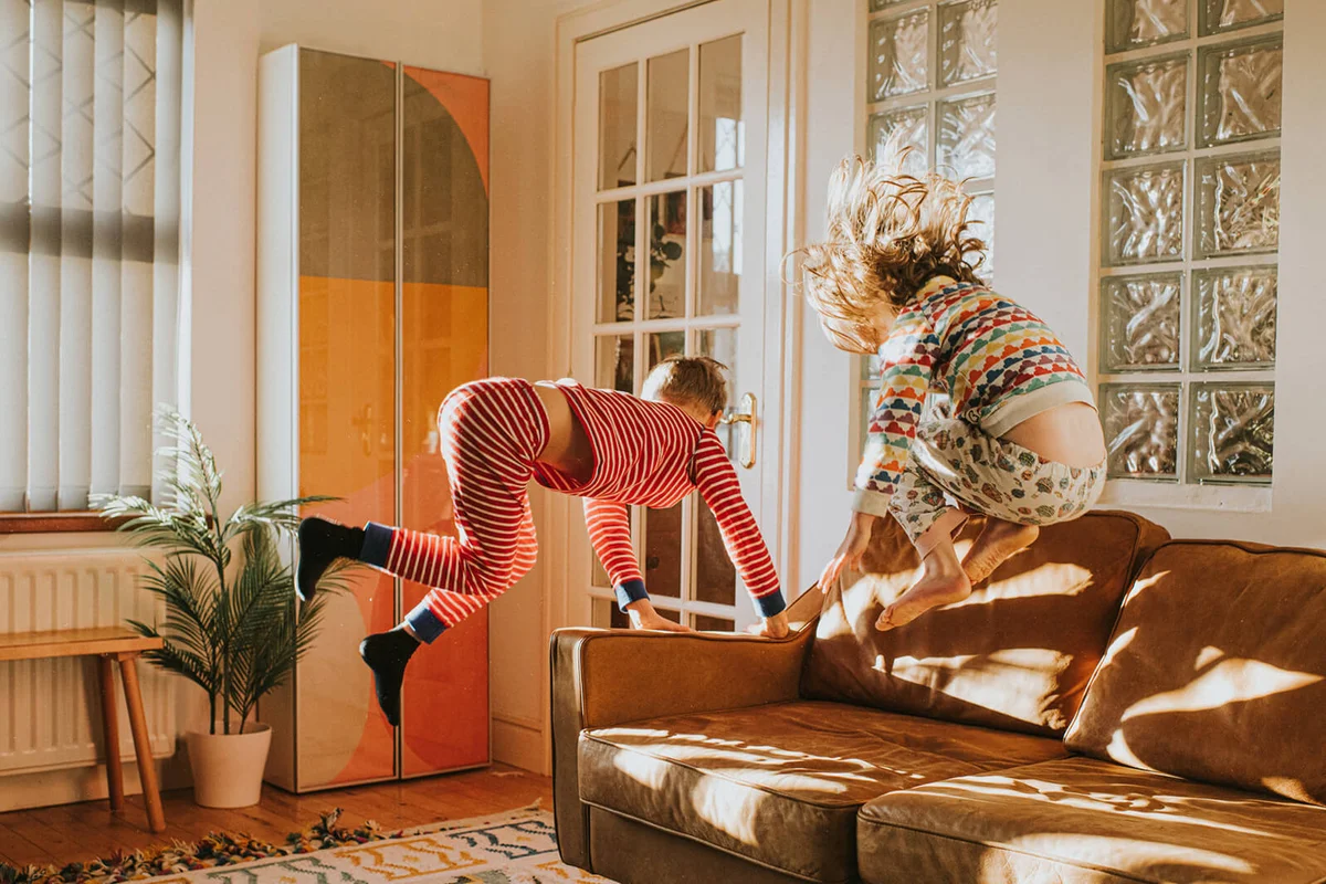Two cute kids wearing pyjamas bounce on a brown leather couch