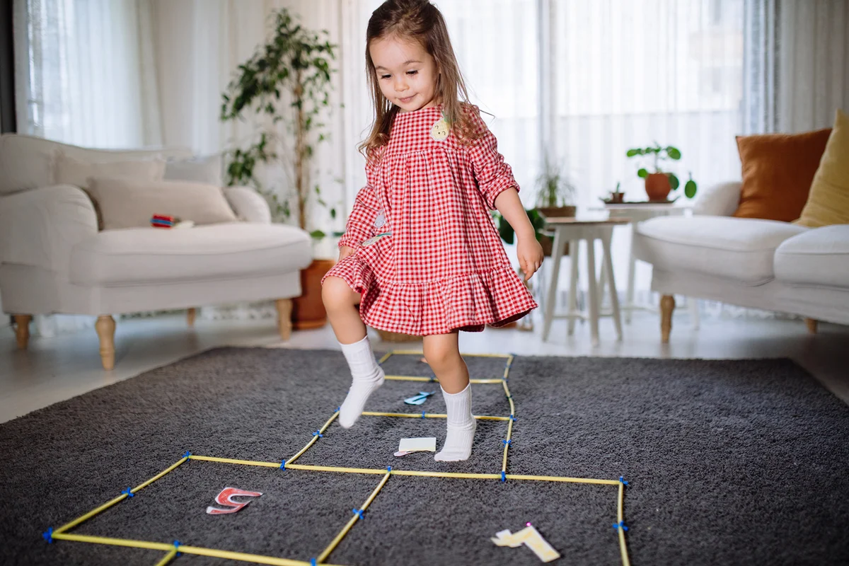 Active cute smiling toddler girl having fun jumping, playing hopscotch at home