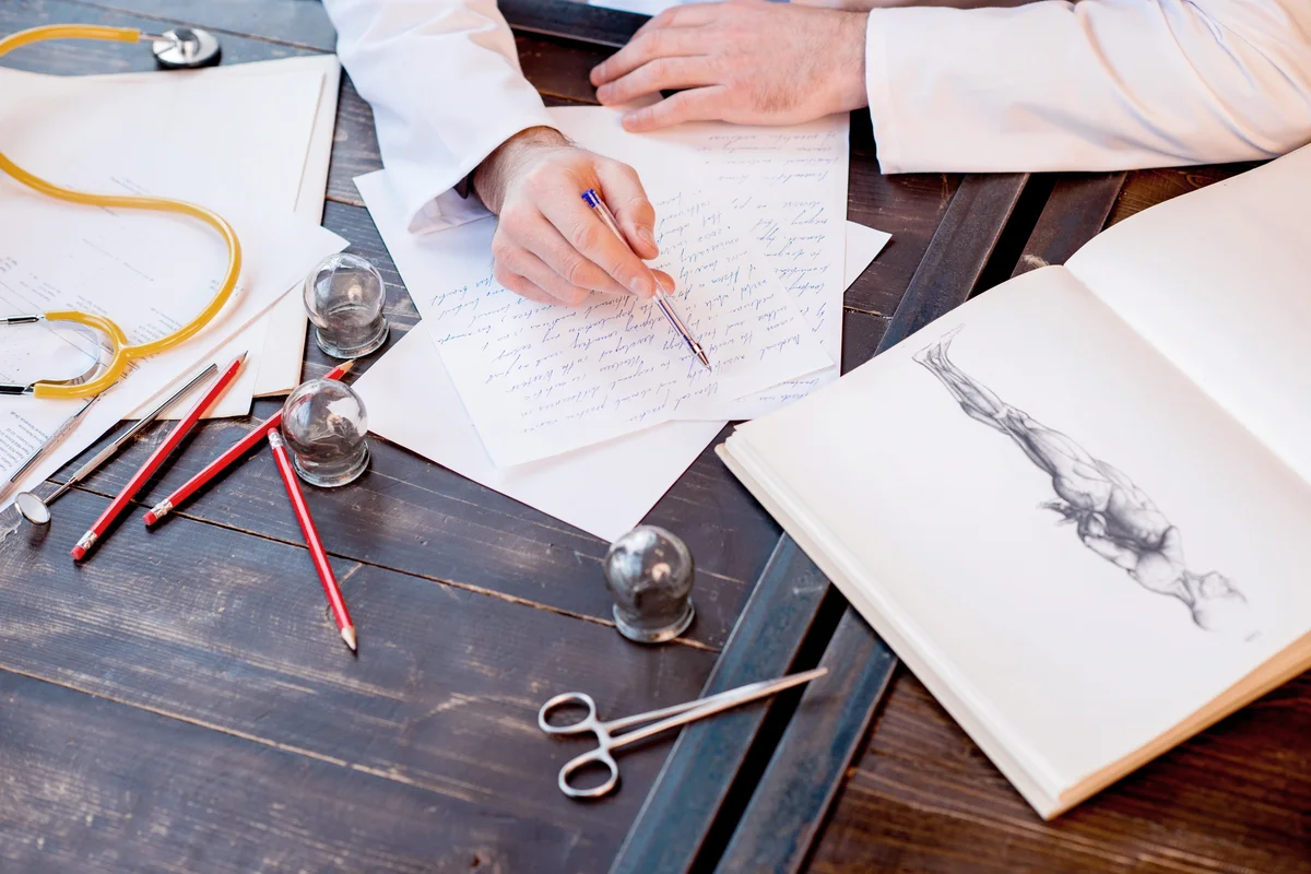 Doctor writing scientific work with antique anatomical book
