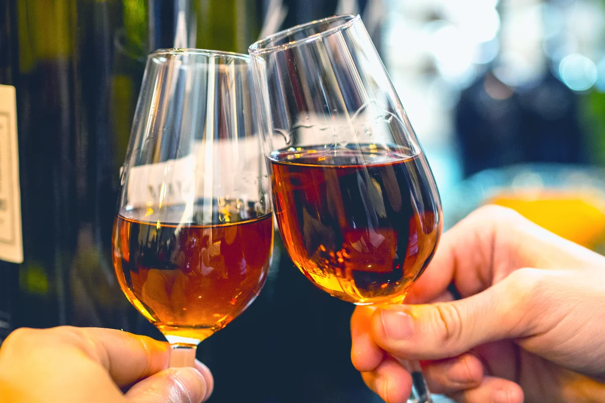 Sherry wine toast at foreground holding by hands and bottles at background