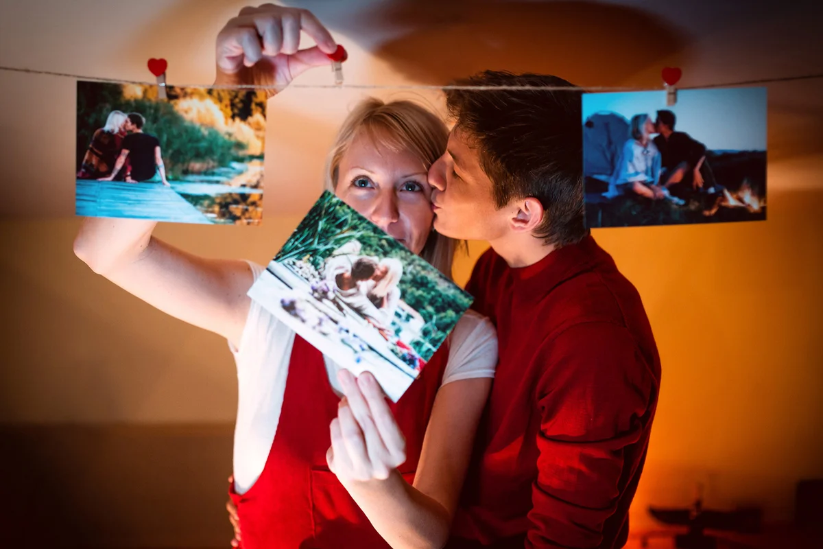 Embracing young couple hanging on their old photos from a travelings on a photo rope