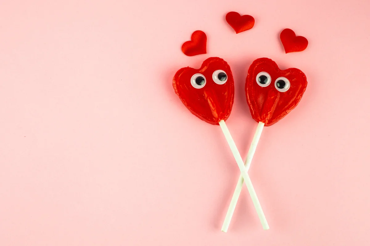 Two red heart lollipops with eyes looking at each other