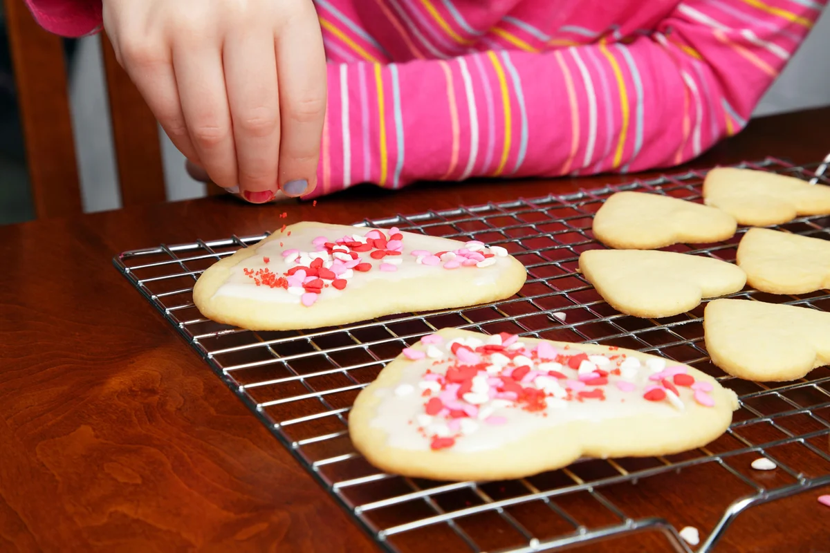 A young girl adds heart sprinkles to her Valentine's cookies