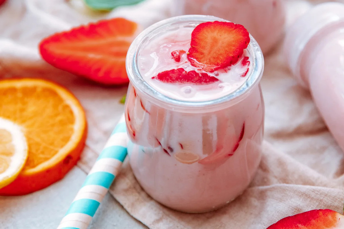 Strawberry yogurt milk shakes with fresh strawberries on a table next to ingredients