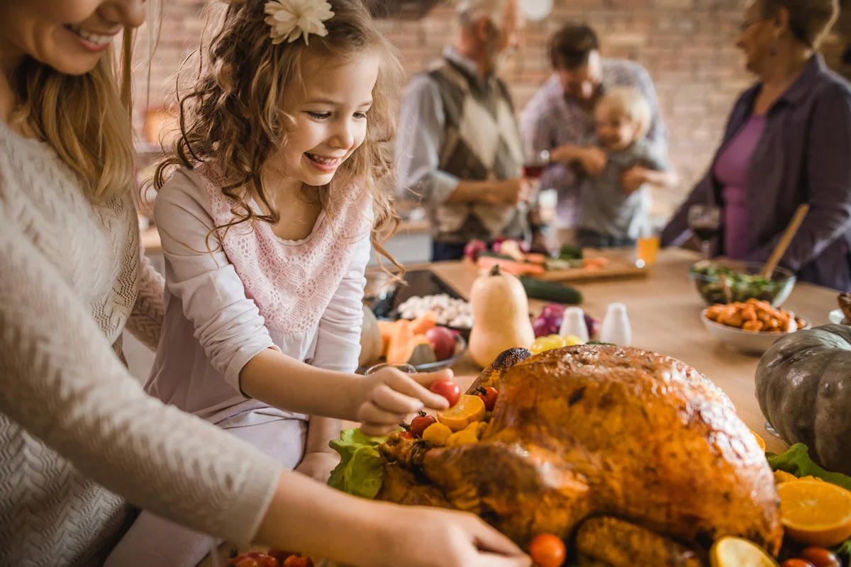 Happy girl and her mother preparing roasted turkey for Thanksgiving dinner
