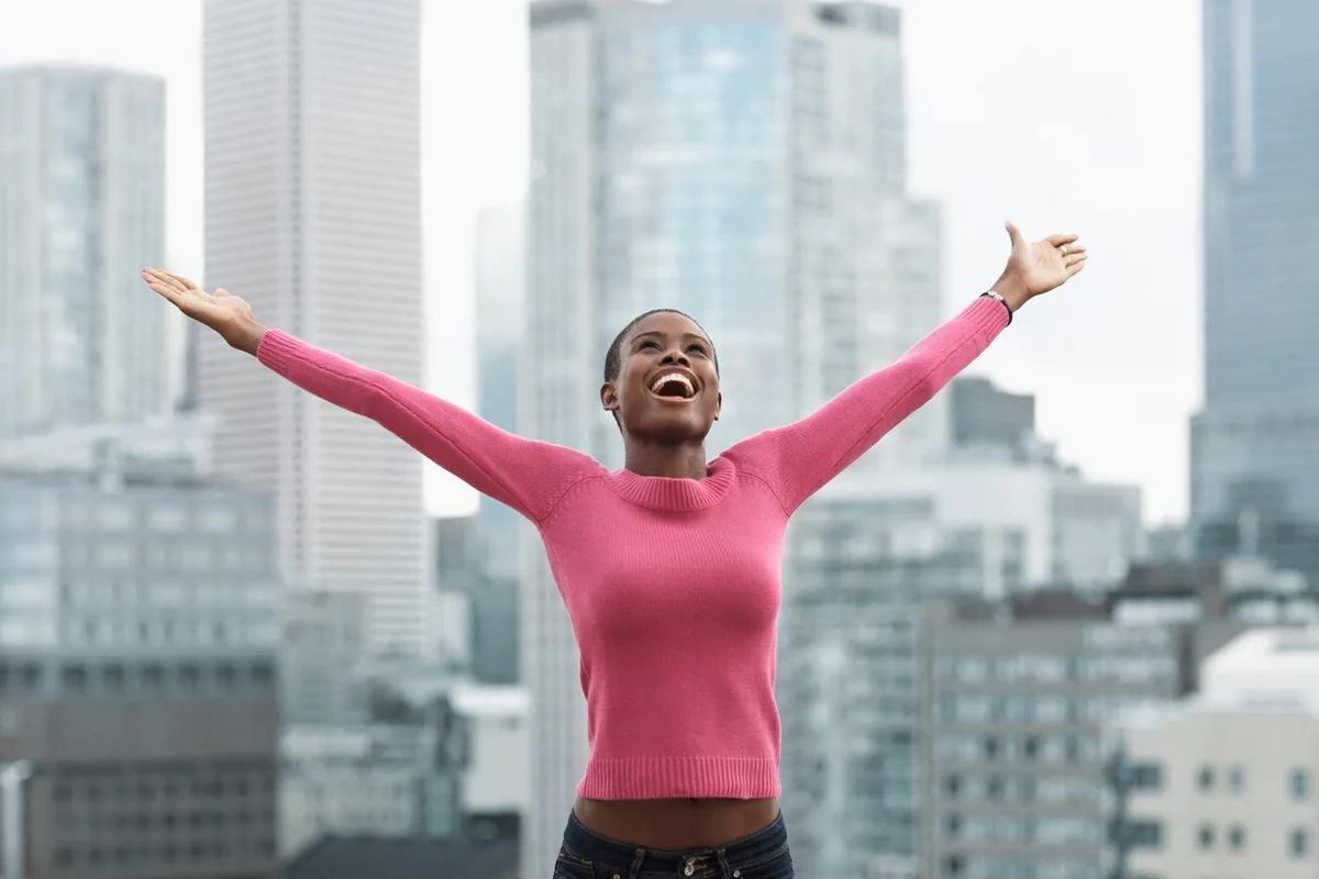 Happy young woman with arms outstretched, cityscape in background