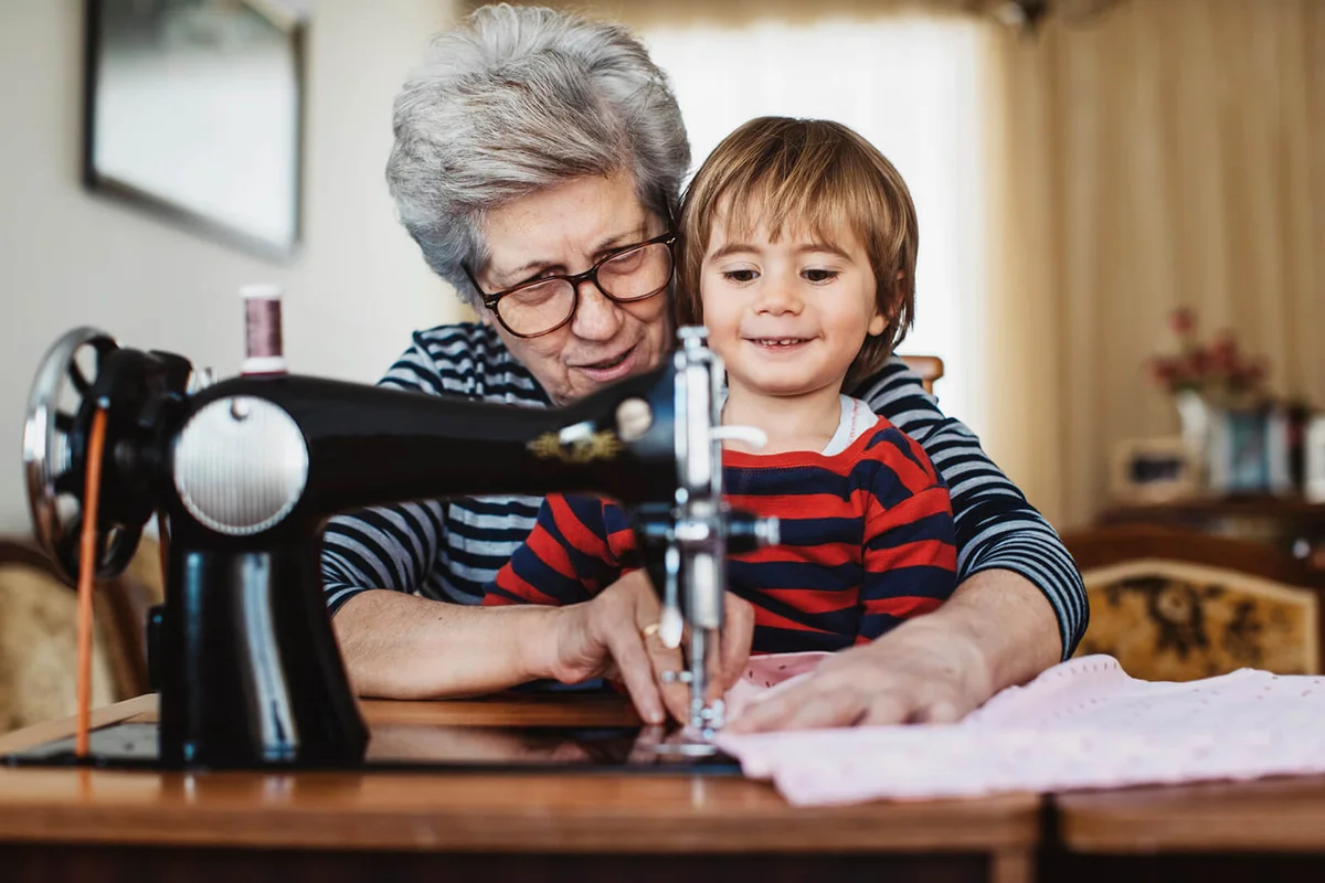 Senior woman with her grandson working on a sewing machine