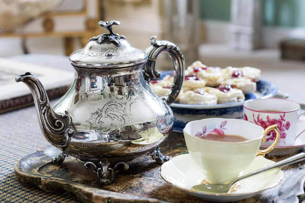 Silver teapot on tray with cups and saucers and scones