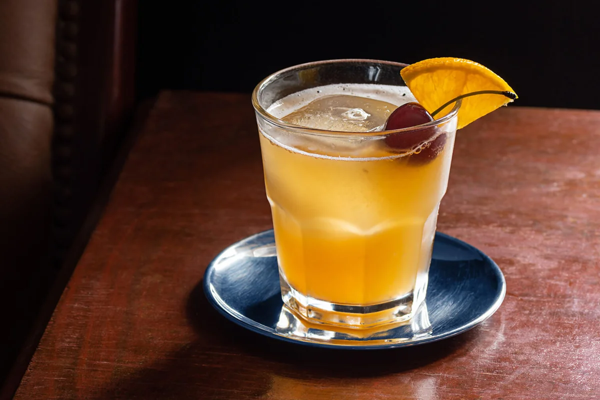 Amaretto Sour Cocktail on the Rocks with Cherry and Orange Garnish in Dark Luxurious Bar