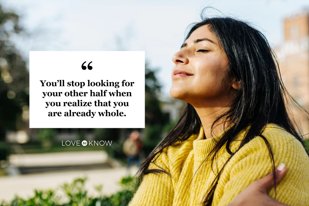 Smiling woman hugging self against sky