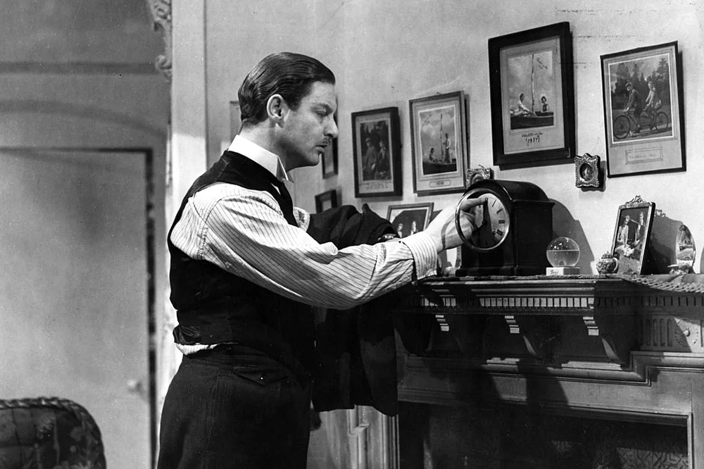 Robert Donat corrects the time on the clock on the mantlepiece