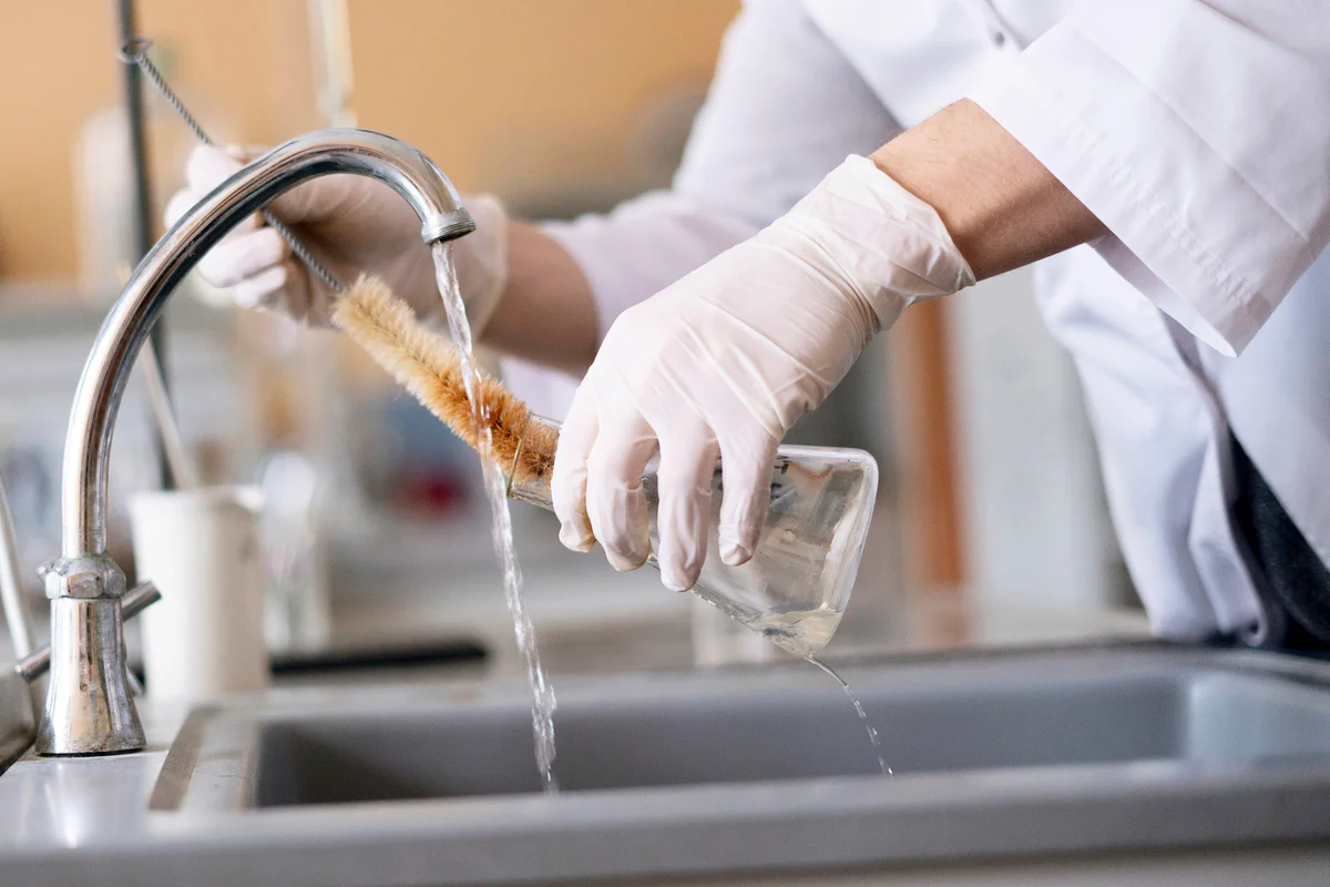 Person hands in gloves cleaning and washing glass flasks
