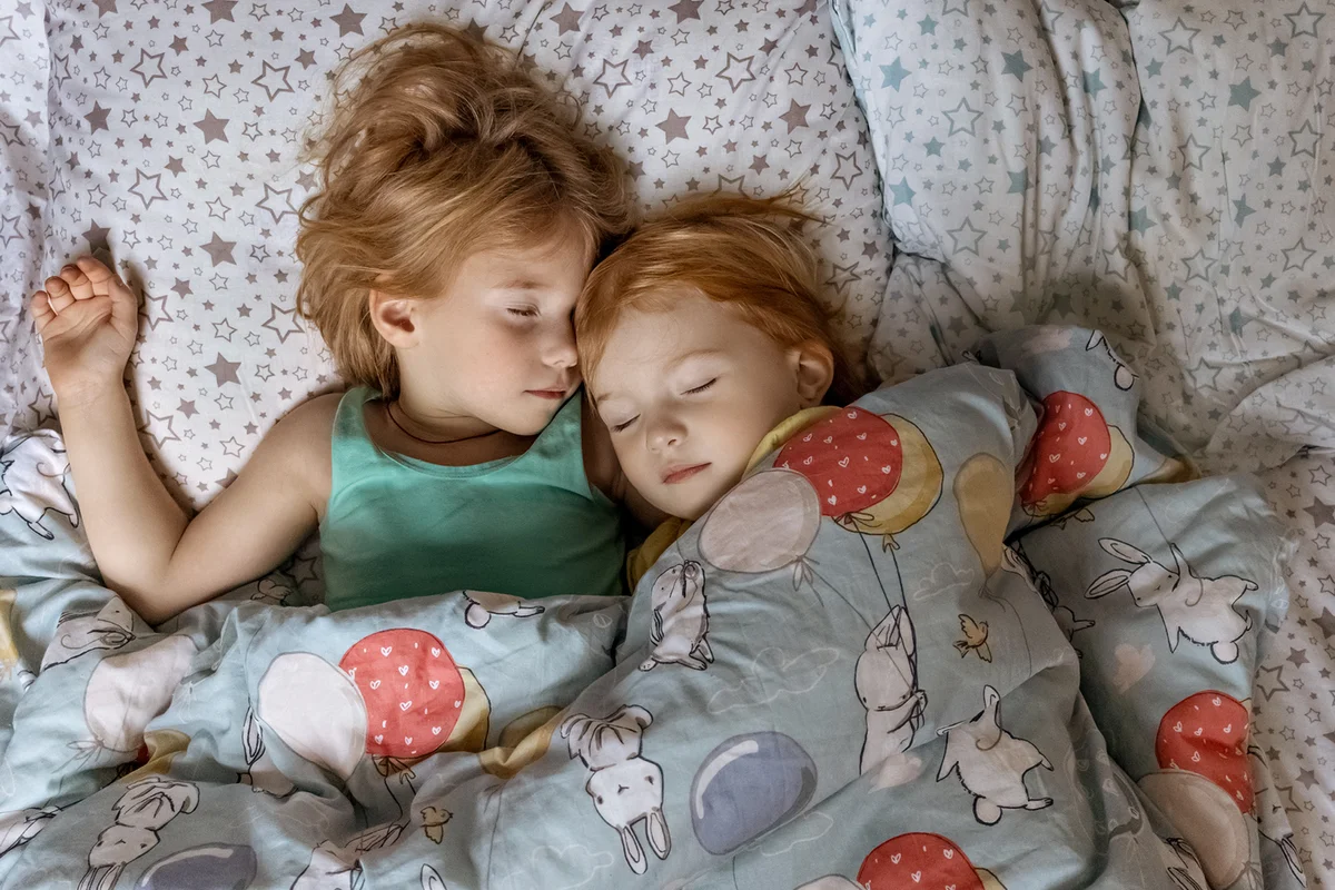 Two little sibling girls sisters sleeping in an embrace in bed under one blanket