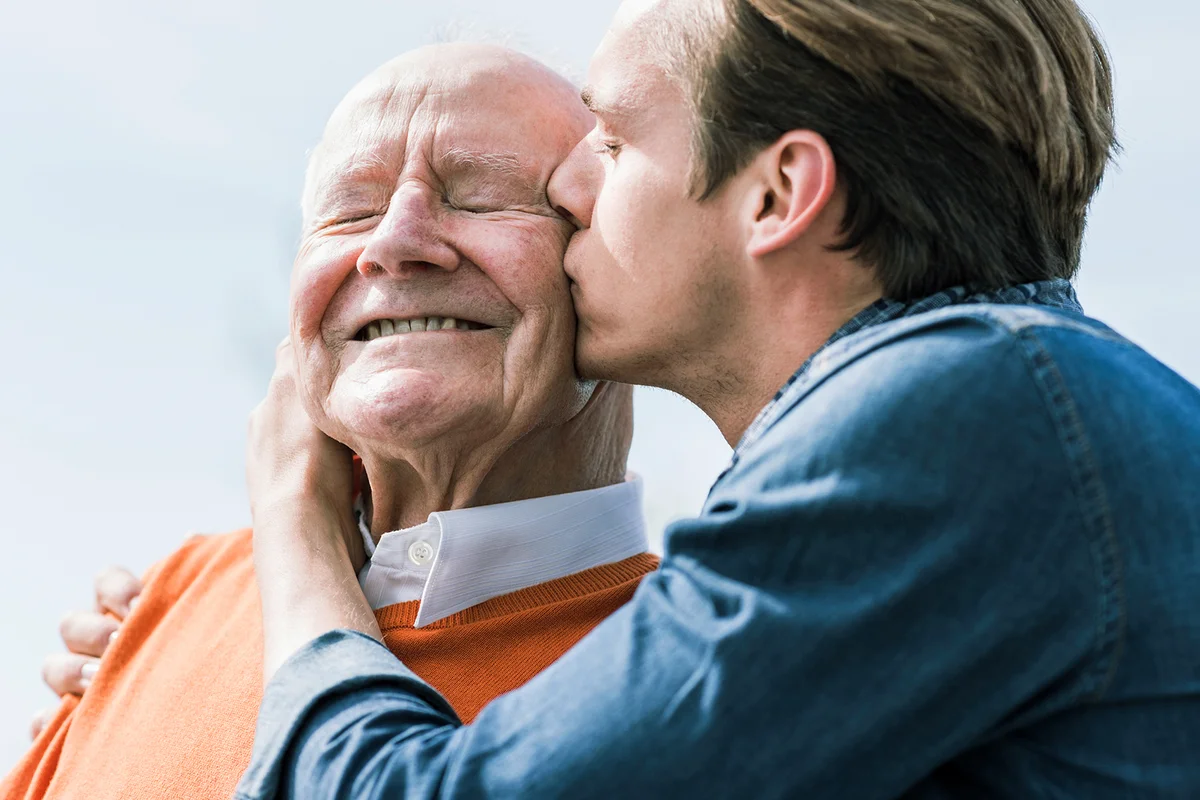 Adult grandson kissing senior man outdoors