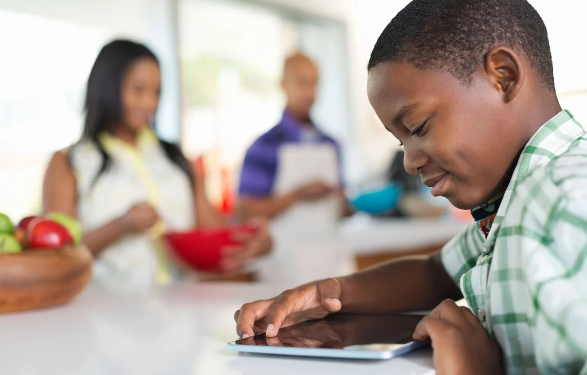 boy using tablet in kitchen with parents supervision