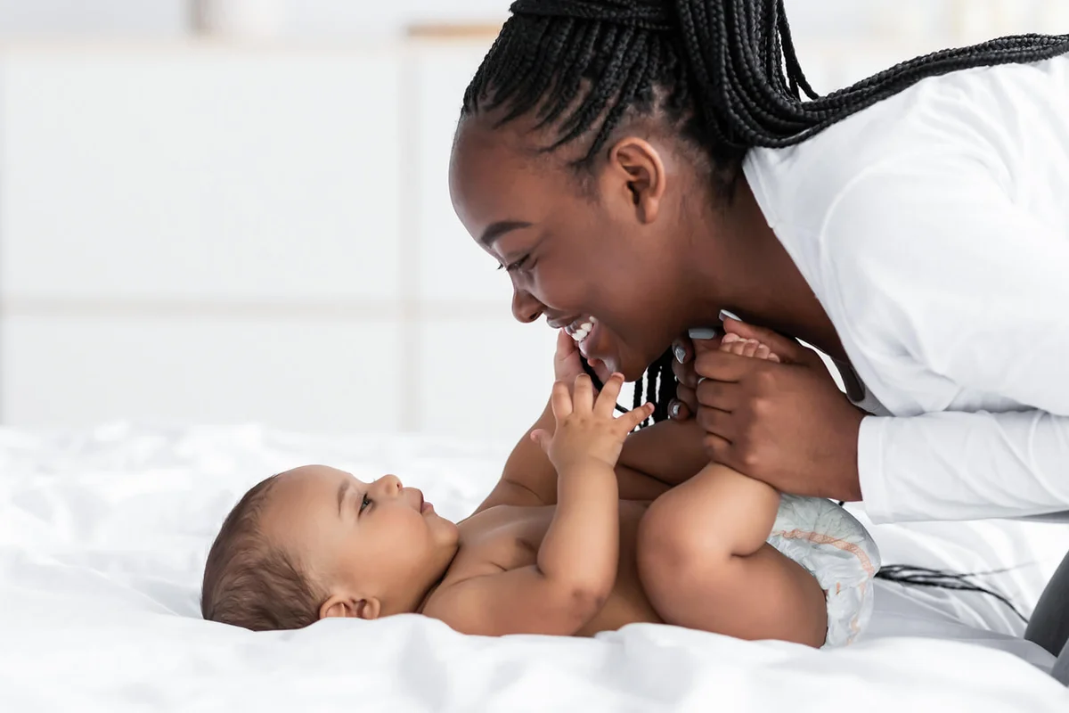 mom playing in bed with her black baby