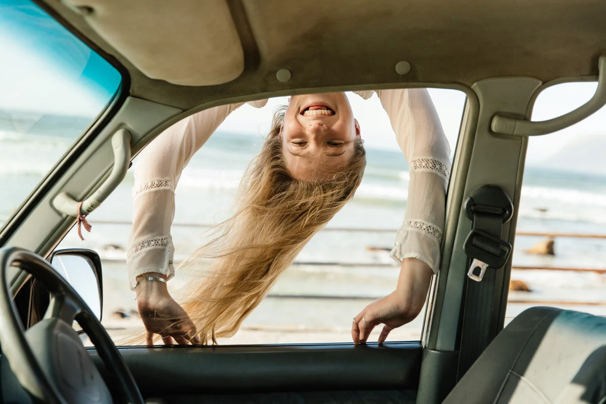 Young woman smiling and peeking into car window from the roof of the car