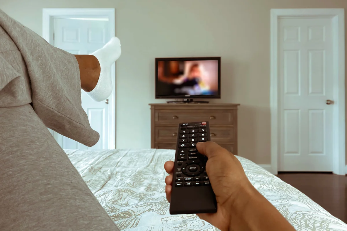 Woman Lounges in Bed Watching TV