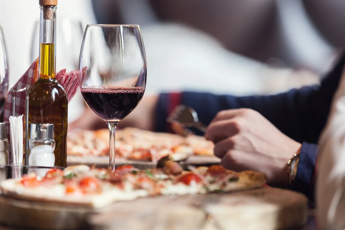 Eating pizza in restaurant, focus on red wine