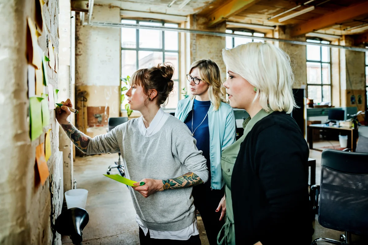 Casual business women having brainstorming and sticking notes on a wall