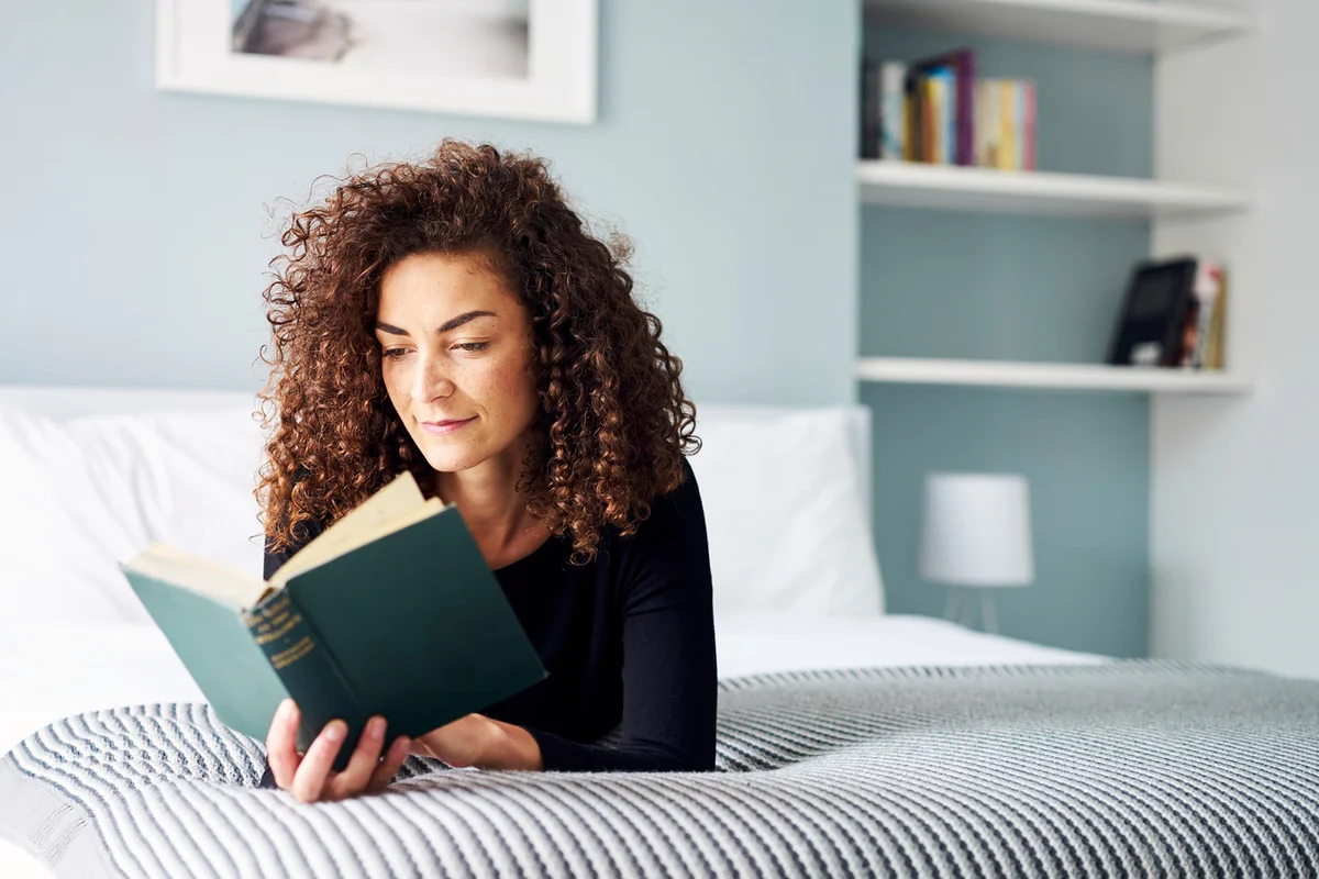 Woman engrossed reading a book at home on the bed in the daytime