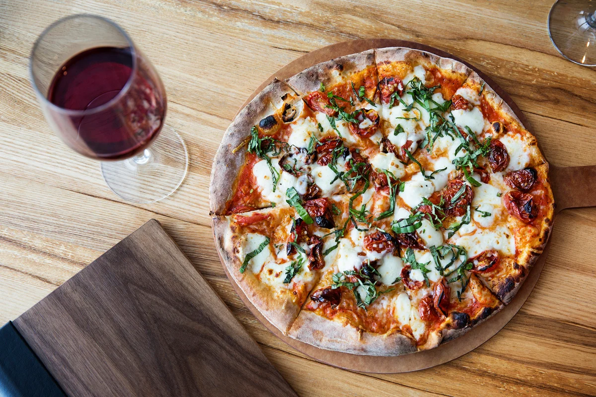Overhead view of fresh pizza with red wine glass on restaurant table
