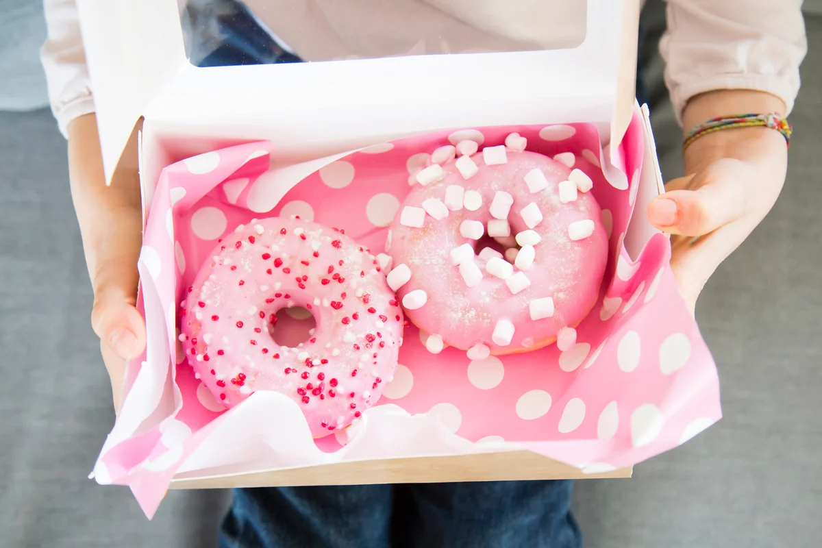 Girl holding box with doughnuts, partial view