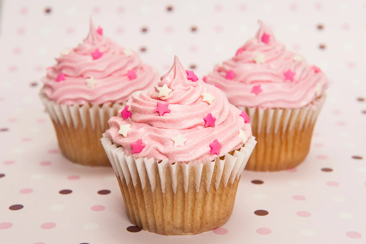 Three pink cupcakes with sparkling frosting and sprinkles