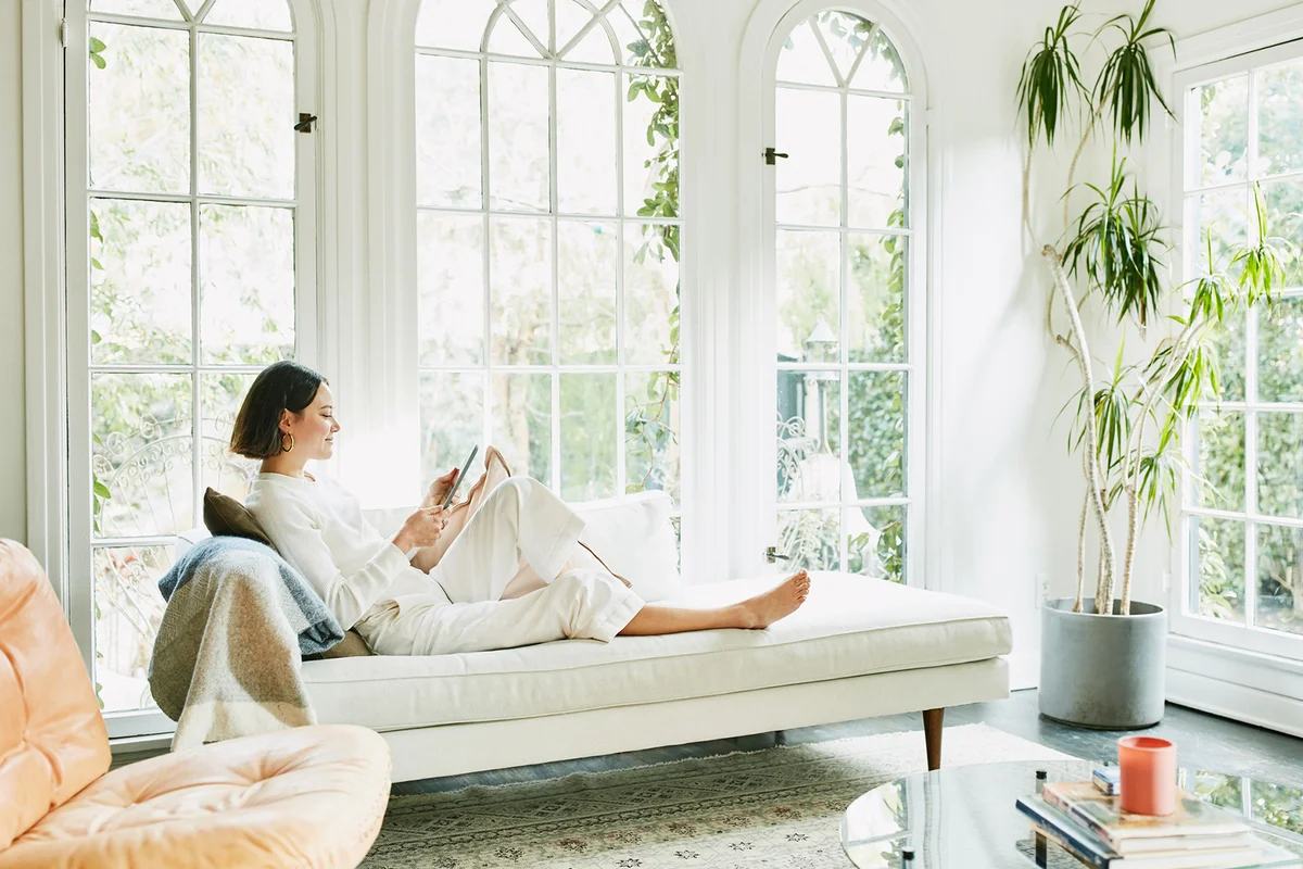 Woman sitting on couch in living room reading on digital tablet