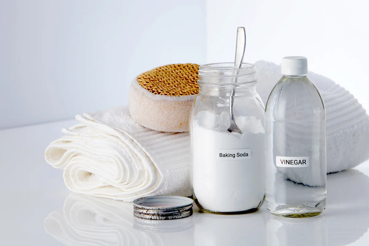 White vinegar and baking soda with scrub sponge and white towel