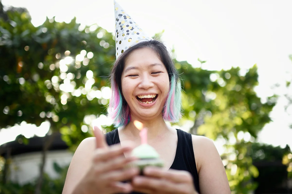 Woman holding a birthday cupcake wearing a party hat